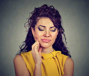 Woman with sensitive tooth ache crown problem about to cry from pain touching outside mouth with hand isolated gray background.